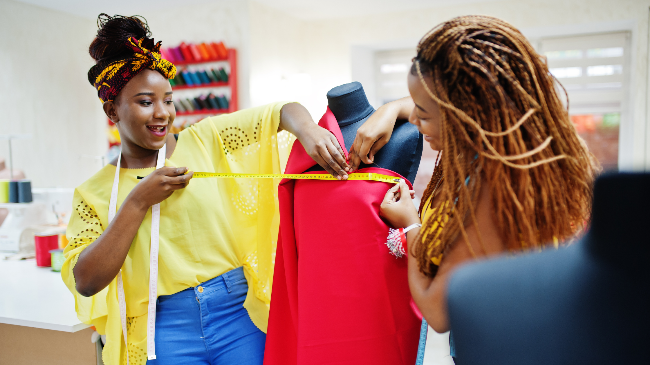 Two black women measuring and designing a dress on a mannequin