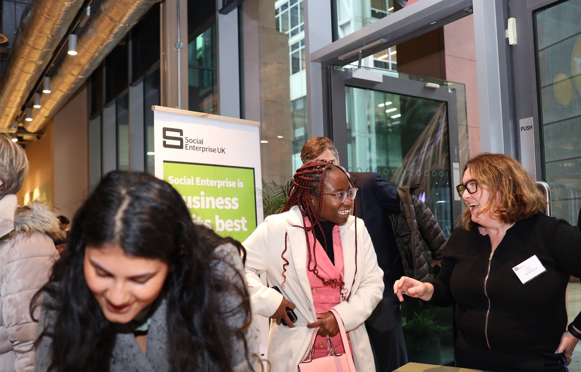 The registration desk at the social procurement meetup event. Featuring three women stood in front of a banner saying social enterprise is business at its best