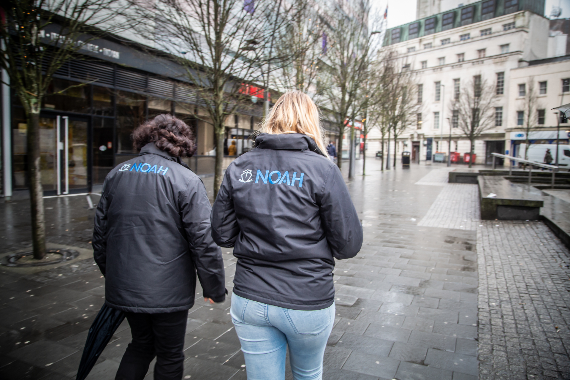 Two women wearing jackets which say the words Noah Enterprise on the back walking down a street