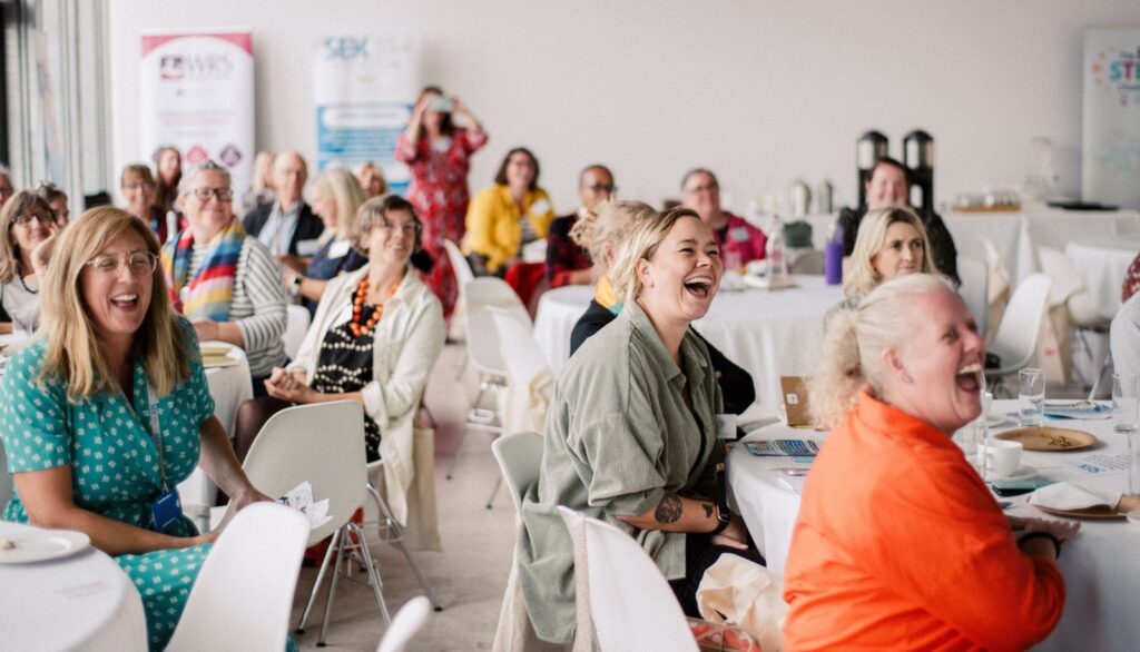a shot of a lively Social Enterprise Kent conference audience sat at tables and laughing