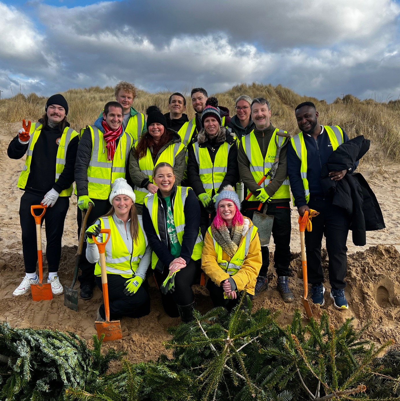 a group of smiling people in hi vis jackets on a beach some holding spades