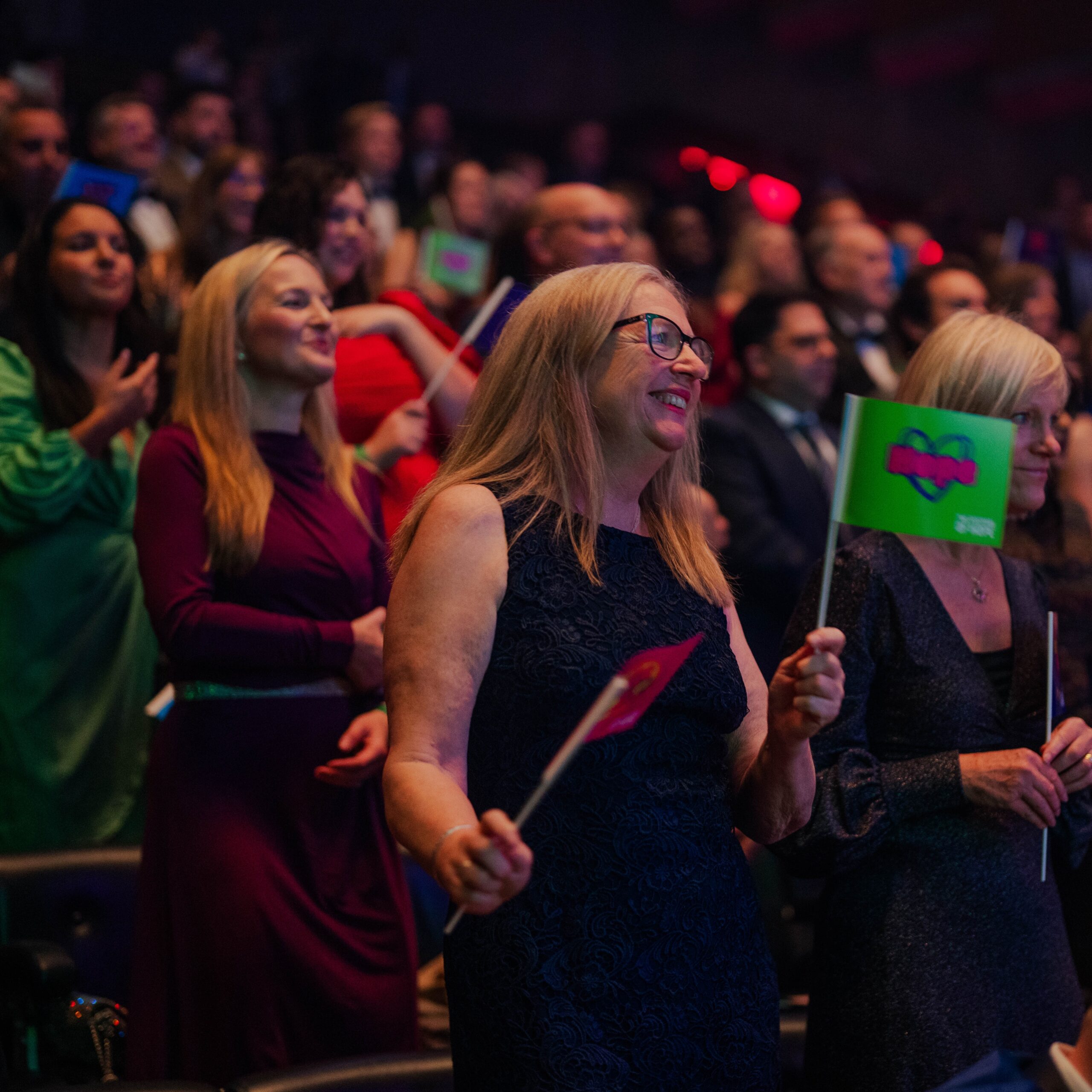 a woman waving a green flag with the word hope written in pink surrounded by other people standing up and dancing atthe Social Enterprise Awards 2026