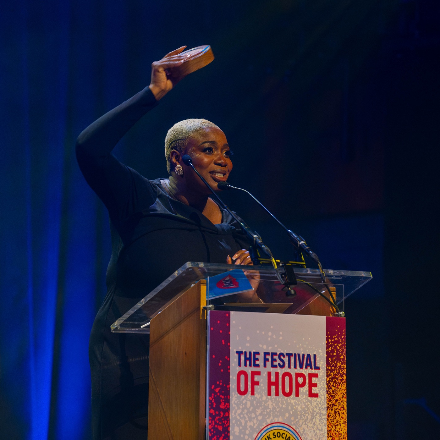 Hannah Oyewole from Young Ladies Club on stage behind a podium holding up her trophy for winning the Social Enterprise Women's Champion Award