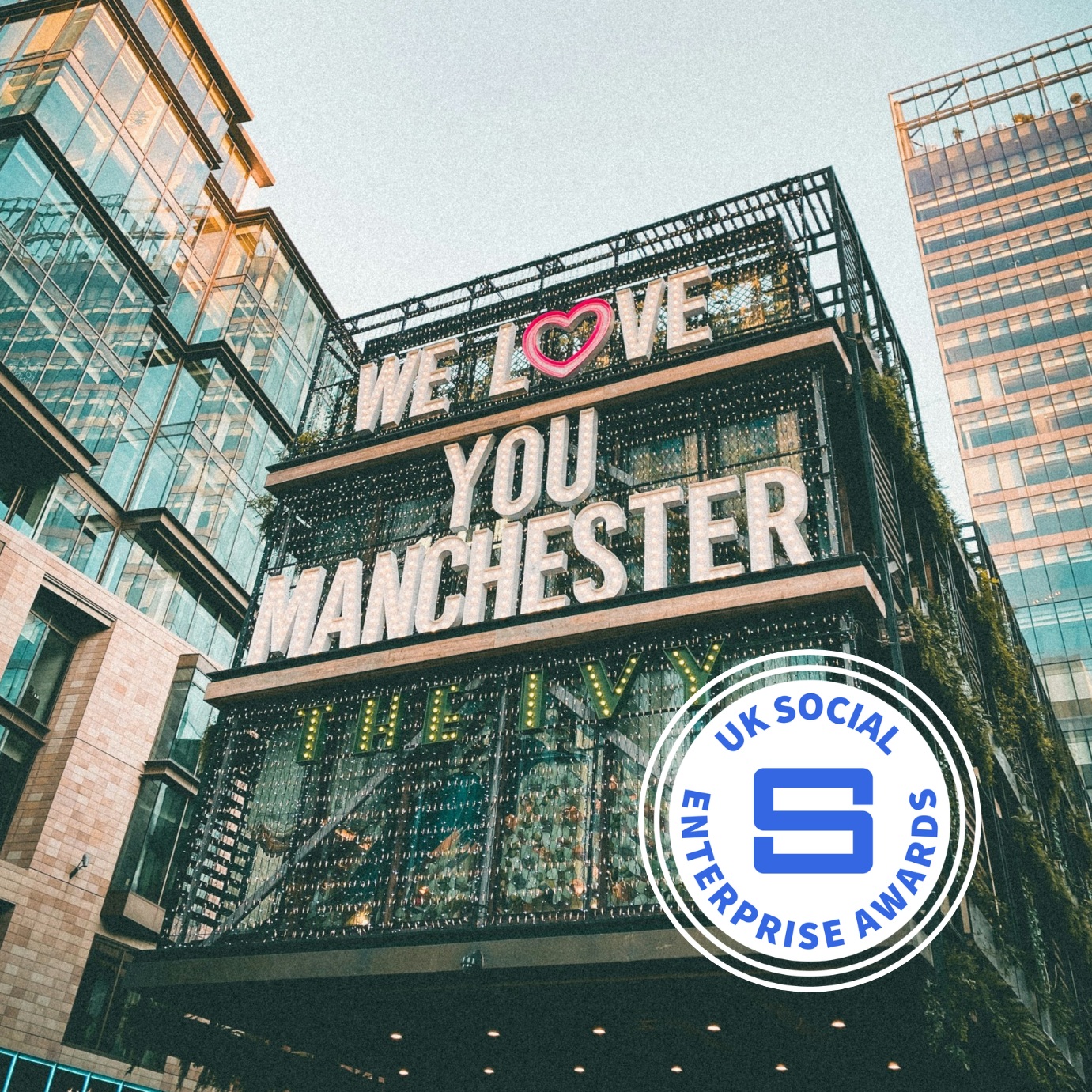 a glass building in Manchester with big block writing on its side stating we love you Manchester. On the bottom right is the Awards logo